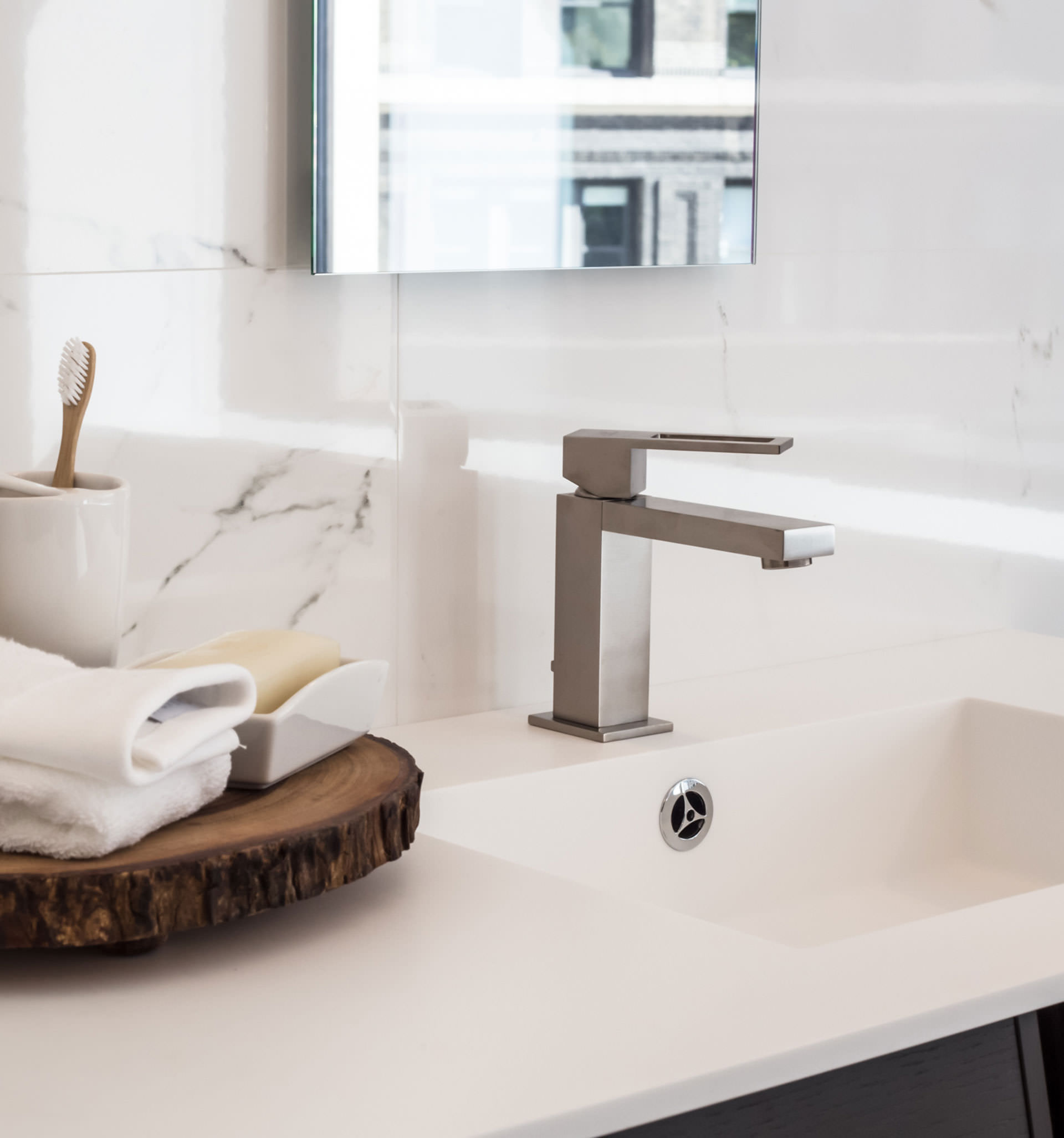 Detailansicht eines weißen Waschbeckens mit Zahnputzbecher, Seifenschale und Handtuch auf einer Holzscheibe