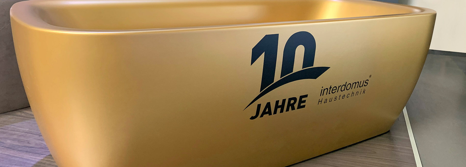 Goldene Badewanne mit Logo zu 10 Jahren interdomus Haustechnik