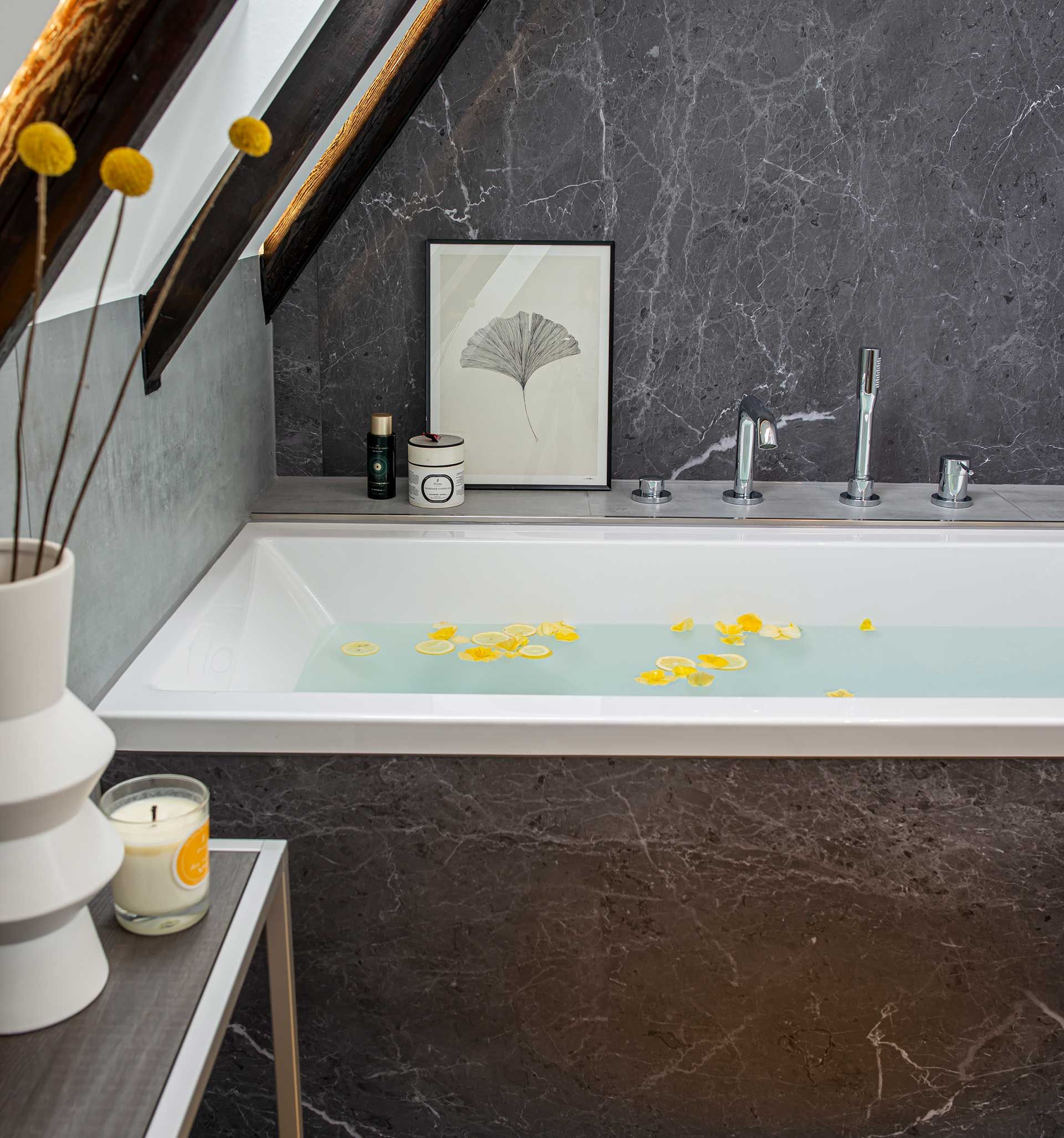 Eingelassene Badewanne unter einer Dachschräge und Wände in dunkler Marmoroptik