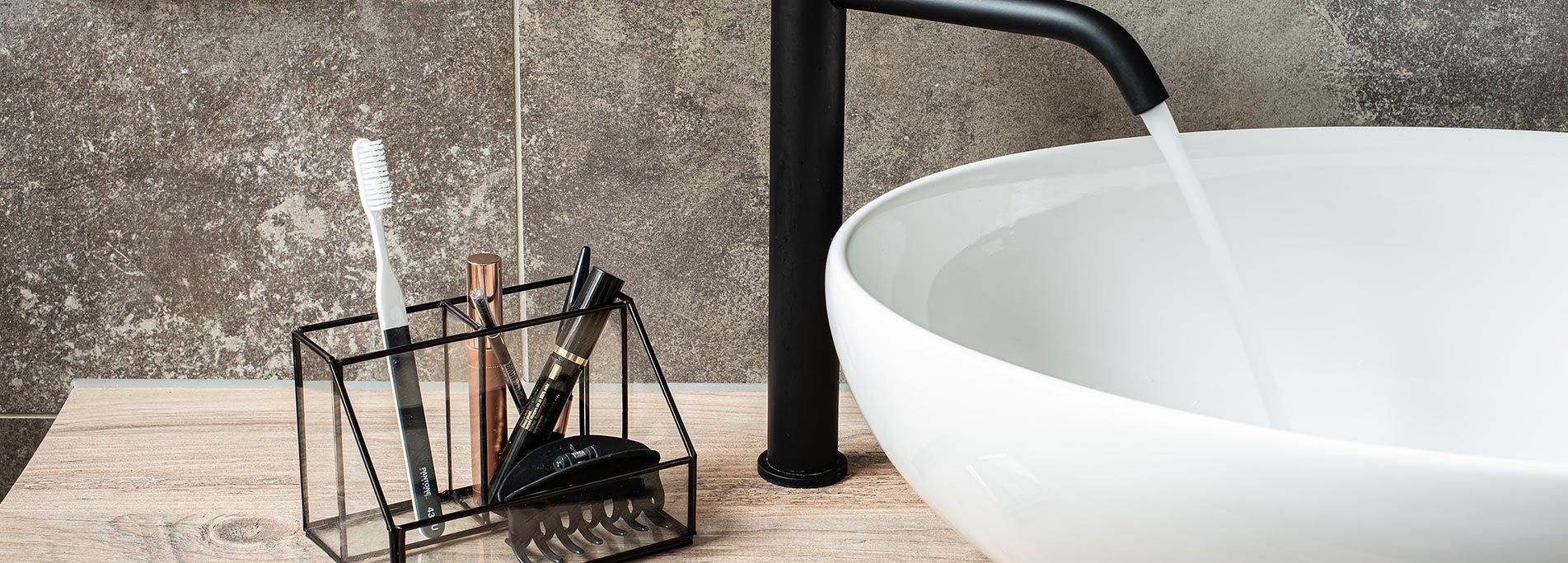 Waschbecken mit schwarzem Wasserhahn, runder Schale und Zahnbürstenhalter.