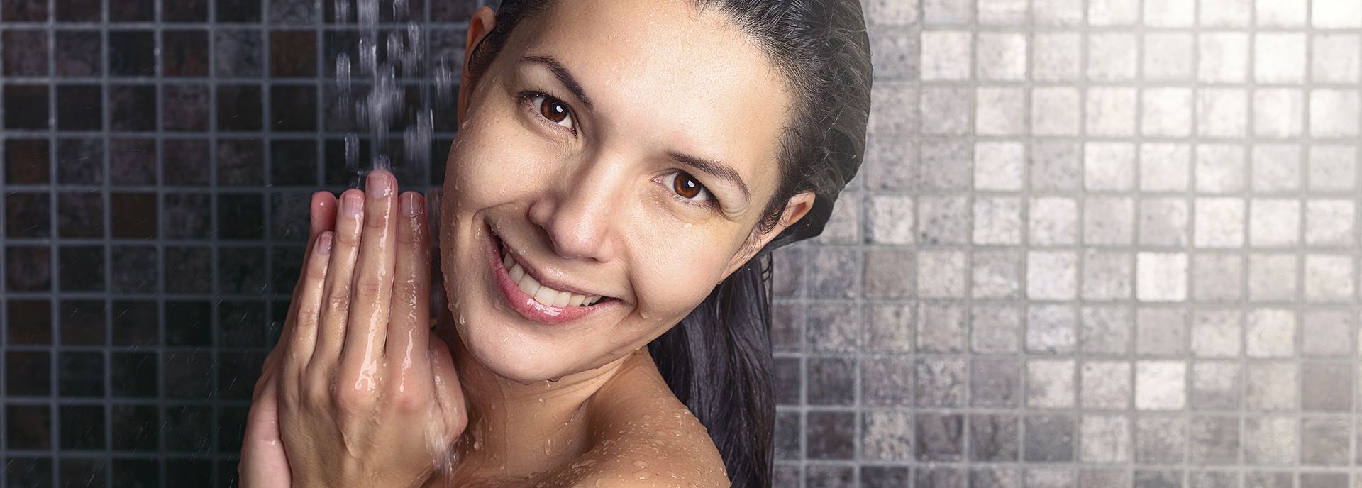 Nahaufnahme einer lächelnden Frau unter der Dusche mit Wassertropfen auf der Haut.