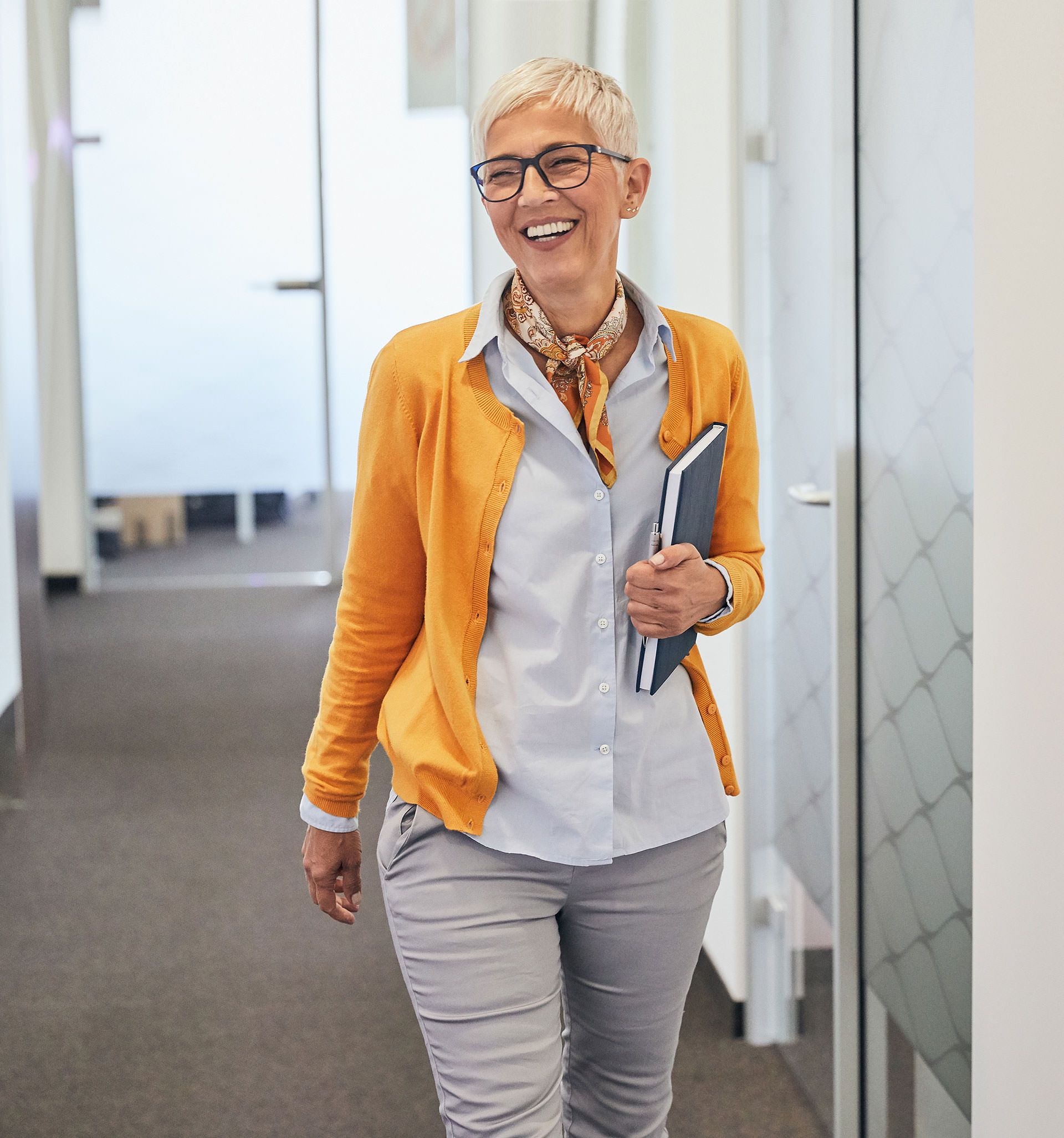 Lachende Geschäftsfrau in gelber Strickjacke im Büroflur.