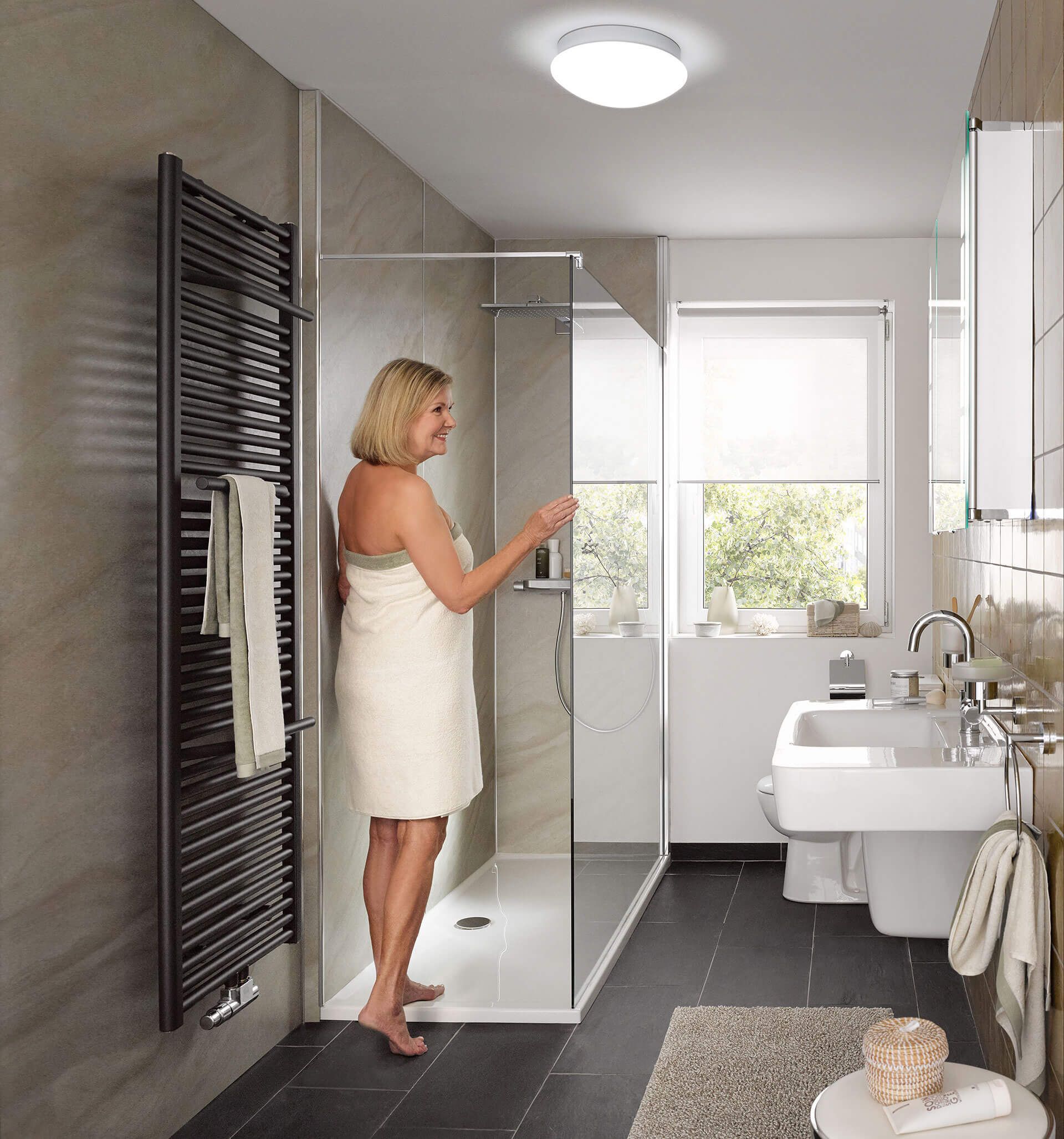 Wir begleiten Sie auf dem Weg zum Traumbad Lächelnde Frau im Handtuch im modernen Duschbereich.