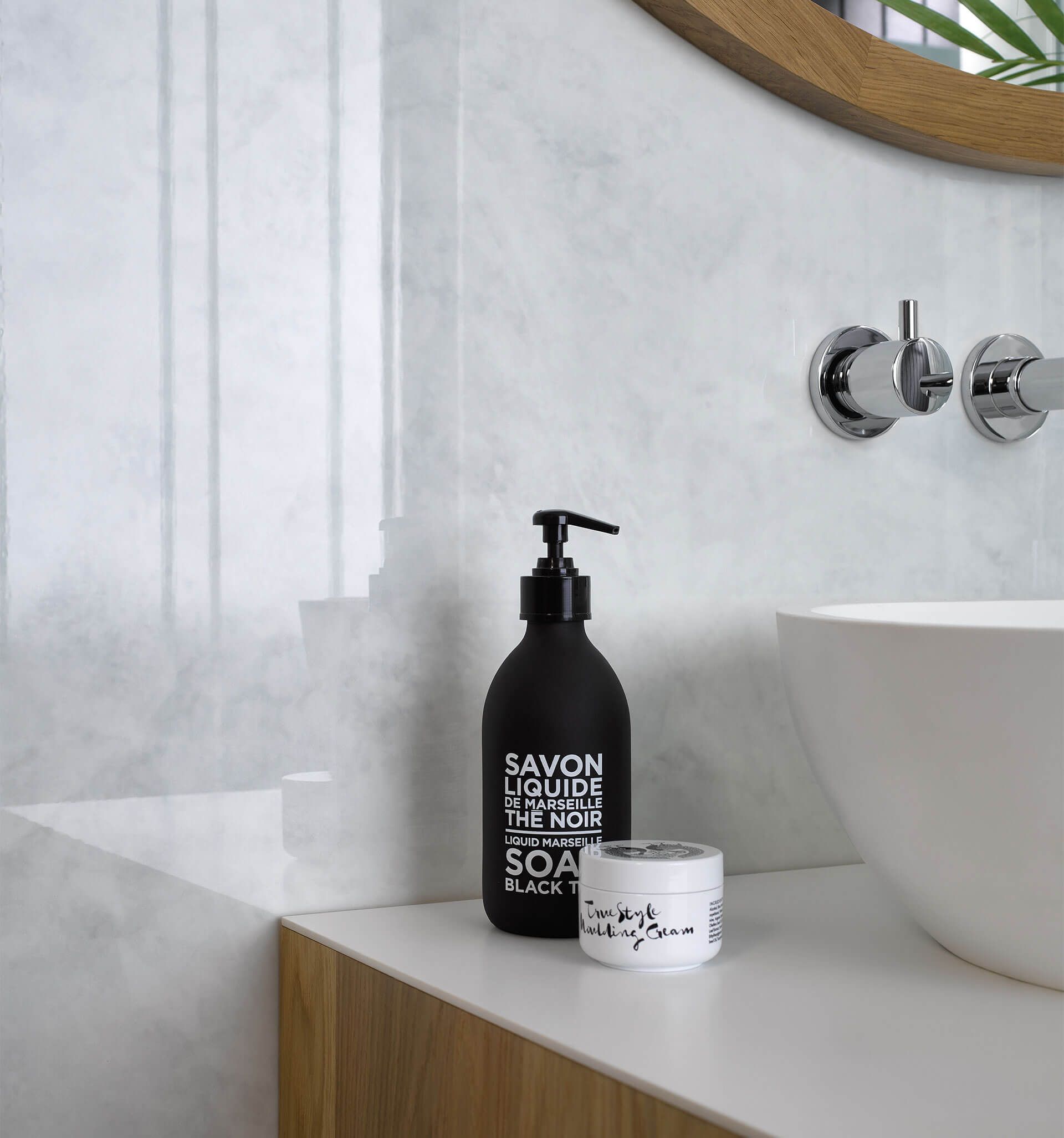 Nahaufnahme eines Waschtisches mit Aufsatzbecken, schwarzem Seifenspender und einer Wand in heller Marmoroptik.