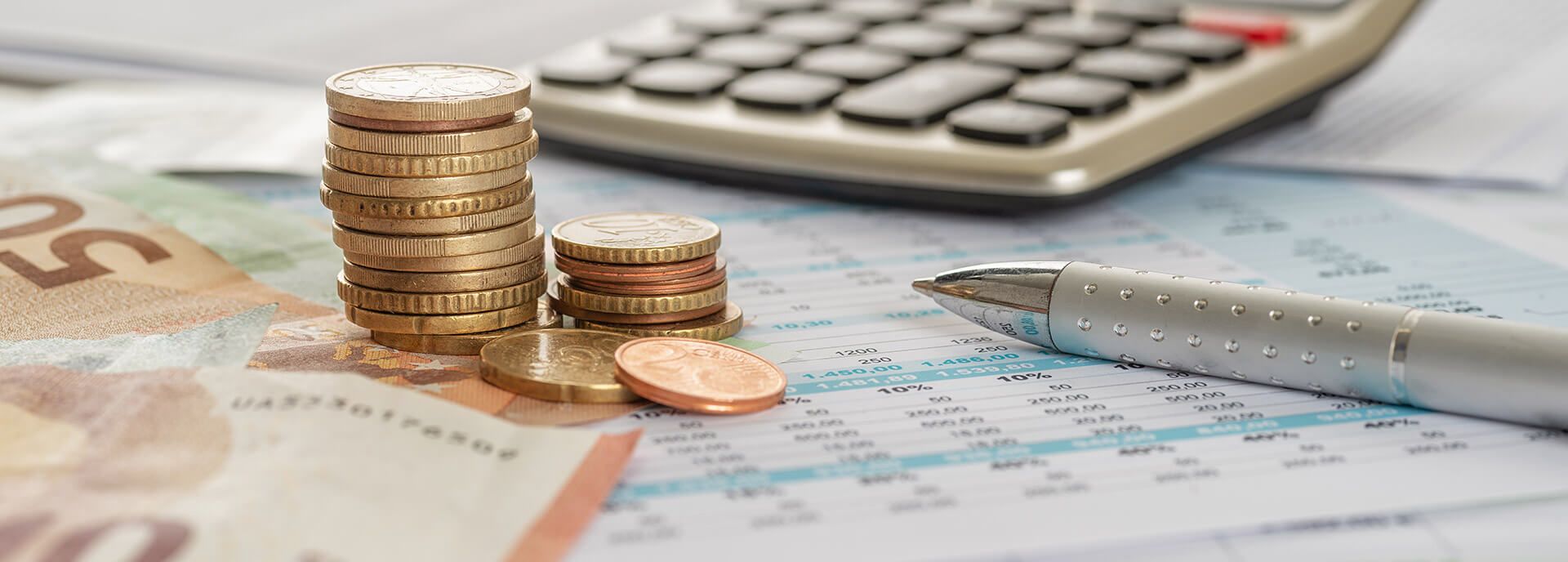 Die Kosten im Blick mit dem Budgetplaner Nahaufnahme: Geld, Rechner und Stift auf einem Zahlenblatt.